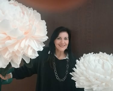 Clara Mennella sorride tra grandi fiori scenografici durante un evento legato al mondo del food & wine.