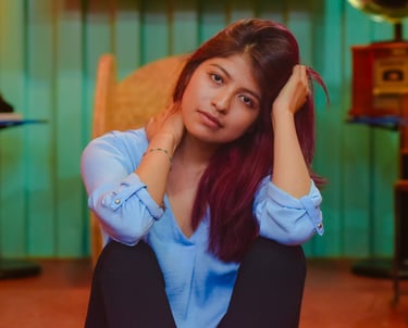 Young woman with long red hair posing in a blue shirt against a teal background.