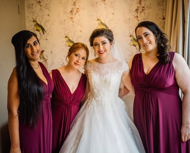 Smiling bride in a lace wedding dress posing with bridesmaids in plum purple dresses.
