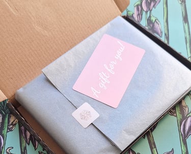 Gift box packaging with grey tissue paper and a pink 'A gift for you' sticker on floral background.