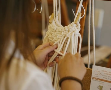 Manos tejiendo pieza de macramé con cordón blanco sobre soporte de madera.
