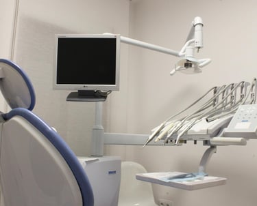 Modern dental examination room featuring an ergonomic chair, overhead monitor, and medical tool console.