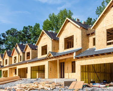 Row of townhomes under construction showing wood framing and OSB sheathing at an active job site.
