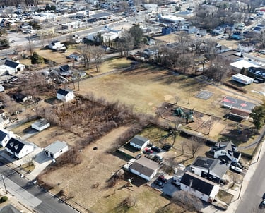 Aerial drone view of a vacant infill lot surrounded by a residential neighborhood and nearby park.