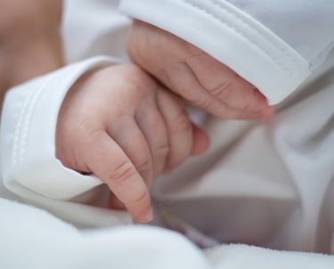 a baby's hand holding a finger on a white blanket