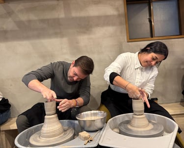 A man and woman shaping clay on spinning pottery wheels during a professional ceramics class.