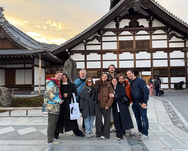 A group of tourists smiling in front of a traditional Japanese temple at sunset in Kyoto.