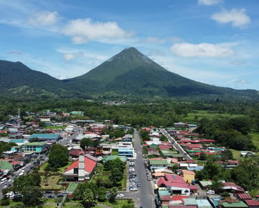 Aerial view of La Fortuna town with the iconic Arenal Volcano in the background under a blue sky.