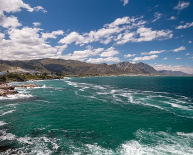 Scenic coastal landscape featuring turquoise ocean waves crashing against rocky cliffs under a bright blue sky.