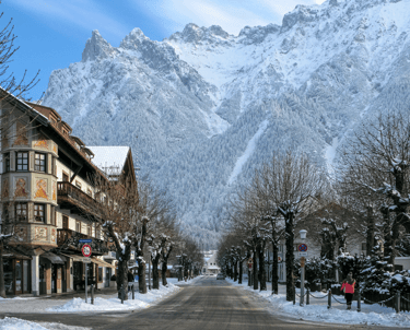 Snow-covered street in Mittenwald, Germany, with traditional Bavarian architecture and Karwendel Alps.