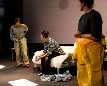 Two brown-skinned people in deep conversation, watched by a third person wearing a hazmat suit