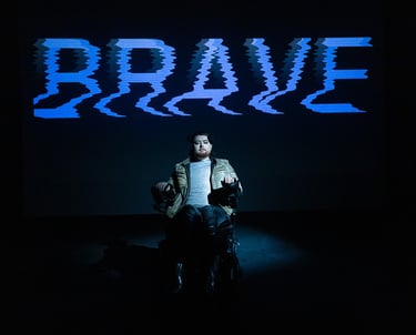 A white electric wheelchair user in a leather jacket in front of the word BRAVE