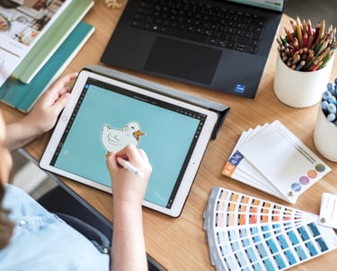 Arbeitsplatz mit Laptop, iPad, Farbkarten und Papierproben.