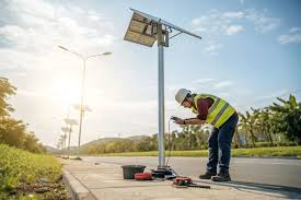 A technician installs solar panels on street lights along a road for sustainable energy.