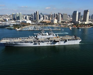 a large Navy ship in the water with a city in the background