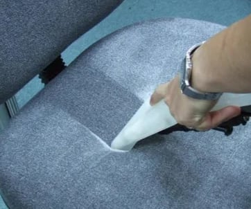 a person cleaning a chair with a vacuum cleaner