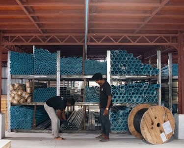 Two men standing in a warehouse with a lot of pipes