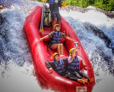 A group of tourists in a red inflatable boat white water rafting down a waterfall in a tropical jungle.