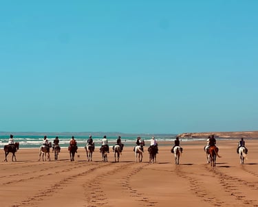 groupe de cavaliers montant à cheval sur une plage immense, avec un ciel d'un bleu éclatant