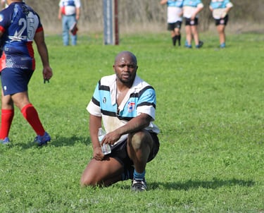 a black man in a striped shirt is kneeling down and holding a rugby ball