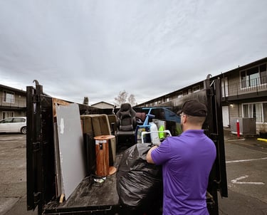 A junk removal professional loading a black dump trailer with furniture and debris for disposal.