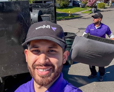 Professional junk removal team loading a mattress into a truck on a sunny residential street.