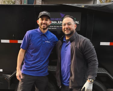 Two professional junk removal specialists standing by a black dumpster trailer.