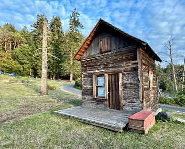 A historic, rough-hewn cabin on the grass.