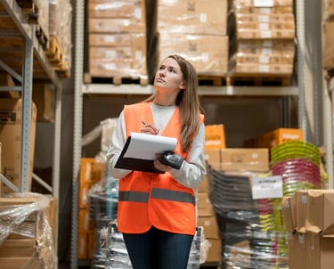 a woman in a safety vest holding a clipboard in a warehouse