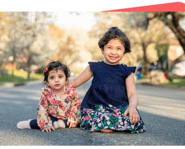 two young girls sitting on the ground in front of a tree
