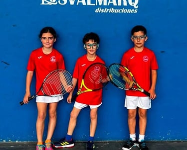 Niños y niñas de la escuela de frontón apoyados en la pared antes de jugar