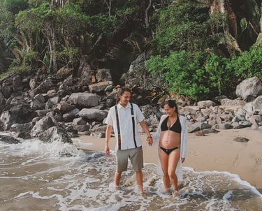 una pareja en la playa, la mujer está embarazada, se observa vegetación en la parte trasera