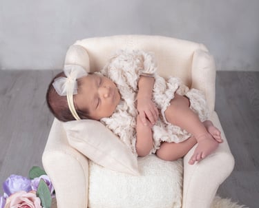 unua bebé recién nacida dormida en un pequeño sillón rodeado de flores