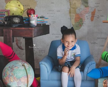 una niña pequeña en un set escolar, con un globo terráqueo y un mapa del mundo atrás de ella
