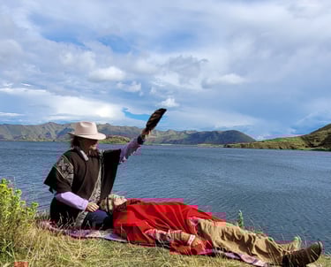 A shaman performs a spiritual healing ritual with a feather fan by a scenic mountain lake.