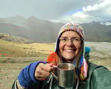 Smiling woman in a colorful hat holding a metal mug during a mountain hike.
