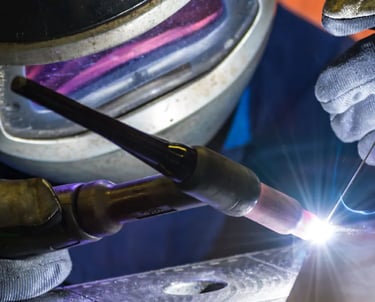 a person welding a piece of metal with a torch in the background