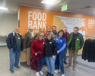 A group of people posing in front of the food back sign while volunteering to pack Christmas food