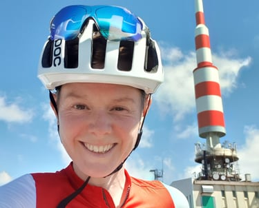 Picture of LIz Hughes dressed in cycling kit, at the top of a mountain, smiling.