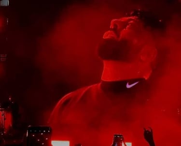 badshah performing on stage under red lights during a live concert with fans recording on phones.