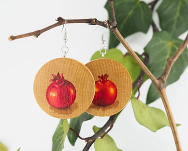 wooden earrings hand painted with pomegranates motif, hanging on branch