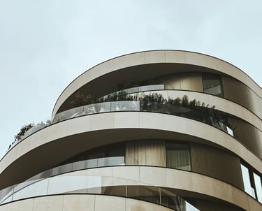 Edificio moderno, redondo, balcones con barandas de vidrio y revestimiento simil piedra y metal