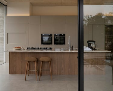 cocina moderna y calida, greige y madera, isla con bacha, anafe y desayunador. Heladera panelada.