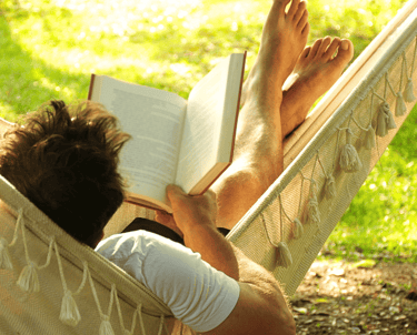 Vīrietis vasarā šūpuļtīklā lasa grāmatu