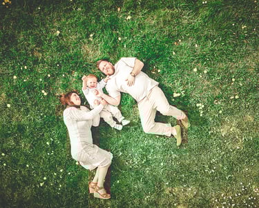Aerial view of a happy family with a baby lying on green grass in a park.