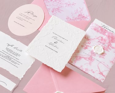 Elegant pink and white wedding invitation suite with floral patterns, wax seals, and deckle edge paper.