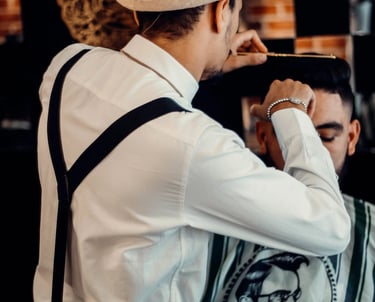 a man in a hat and suspender tie dyes a man's hair