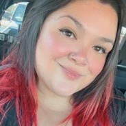 Smiling woman with dark hair, red highlights, and a nose ring in a selfie inside a car.