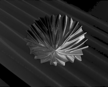 A decorative pleated metal bowl with a textured sunburst pattern on a dark ribbed surface.