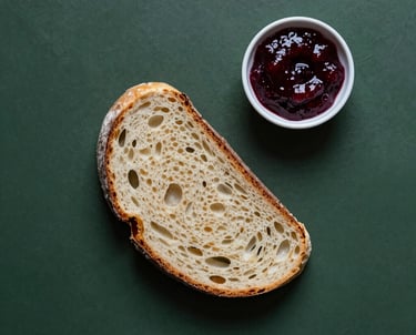 Artistic top-down photo of a dark forest green table with a single slice of sourdough bread and a small bowl of deep red jam, minimalist style.